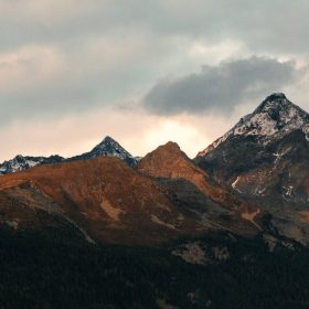 Breathtaking view of mountain peaks adorned with snow under a cloudy sky at dusk.